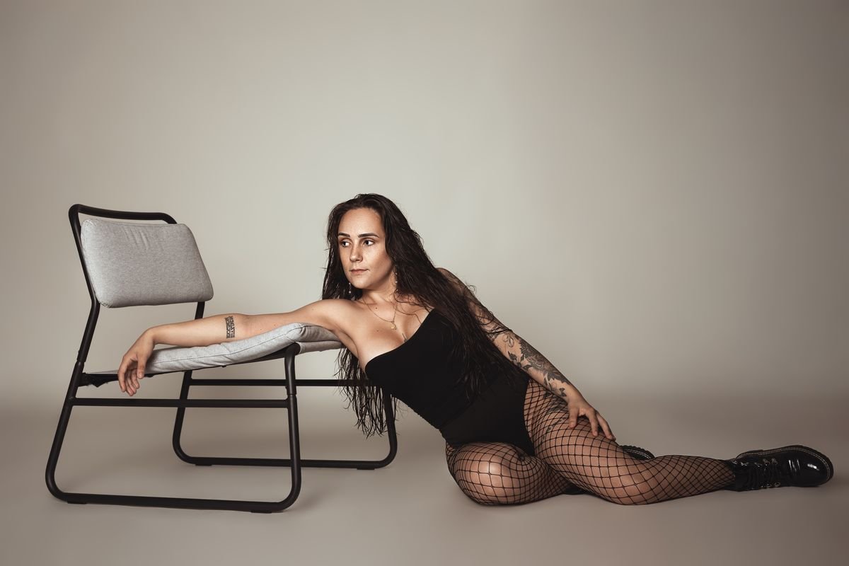 Femme assise au sol près d'une chaise, regard vers l'objectif